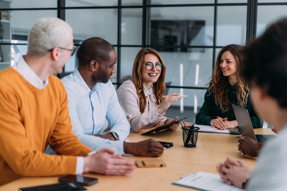 En grupp affärspersoner med olika etniskt ursprung sitter runt ett konferensbord i ett modernt styrelserum och för en engagerad diskussion. 